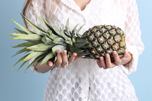 The Asian woman hand holding pineapple in the blue background.
