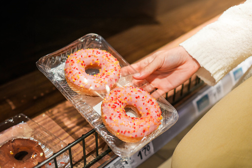 Female hand taking a pack of delicious pink frosting donuts with sprinkles in plastic tray