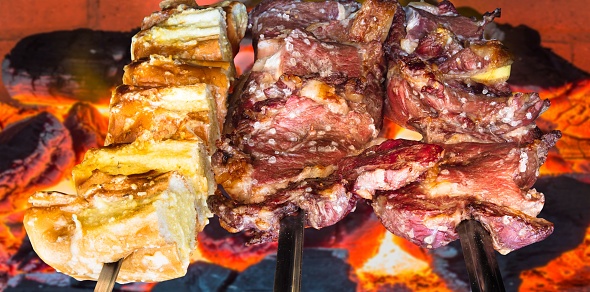 A closeup of a barbecue with grilled beef seasoned with coarse salt and garlic bread.