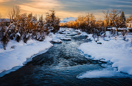 Beautiful view of partially frozen stream in Colorado at sunset; mountain and sunset sky in background