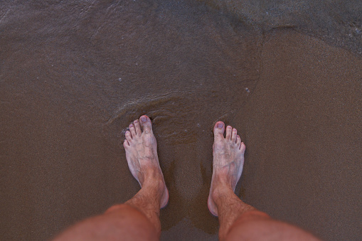 Male feet on sea sand
