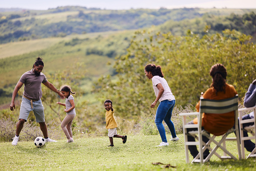 Happy African American family having fun while playing with soccer ball at grandparents' backyard. Copy space.