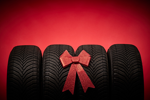 Car tires, new tyres, winter wheels isolated on red christmas background with bow ribbon present.