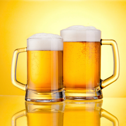 Two Mugs of fresh beer with cap of foam, isolated on yellow background