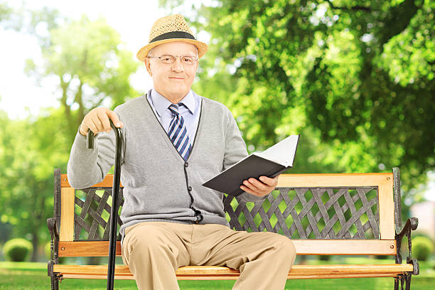 istock Senior man sitting on bench and reading book, in park 181610824