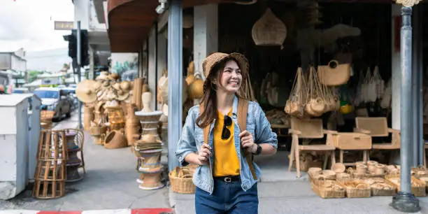 Photo of Young female tourist walking across the street and looking at camera while traveling in local market