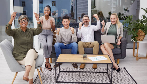 Full body portrait of diverse group of business people cheering while sitting in the office at night. Team of professional workers celebrating beating a deadline while working late in the workplace retrato de cuerpo entero de un grupo diverso de gente de negocios animando mientras están sentados en la oficina por la noche. un equipo de trabajadores profesionales celebrando haber superado una fecha límite mientras trabajan hasta tarde en el lugar de