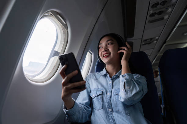 pessoas asiáticas do sexo feminino a bordo, janela do avião, usando celular e fone de ouvido enquanto no avião - room service audio - fotografias e filmes do acervo