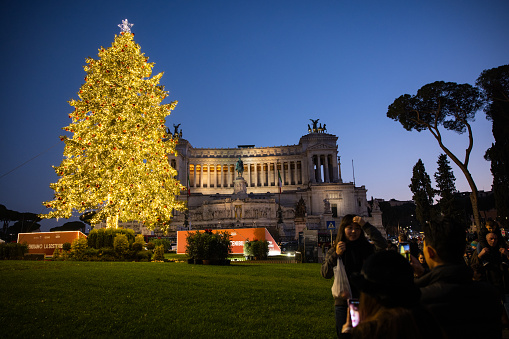 Rome, Italy - December 25, 2022: Christmas tree in Piazza Venezia, with Christmas decorations and lights, in front of the National Monument Altare della Patria on December 25, 2022 in Rome, Italy. Cars and traffic complete the composition.