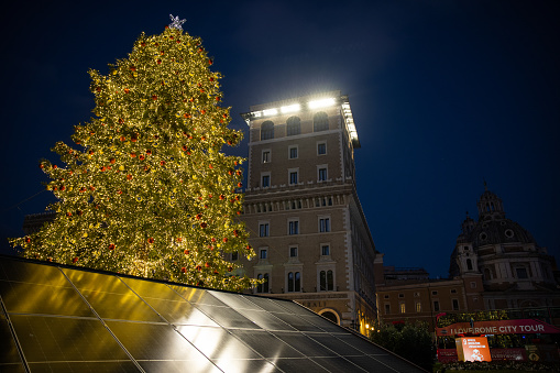 Rome, Italy - December 25, 2022: Christmas tree in Piazza Venezia, with Christmas decorations and lights, in front of the National Monument Altare della Patria on December 25, 2022 in Rome, Italy. The tree is powered by solar panels sustainable energy