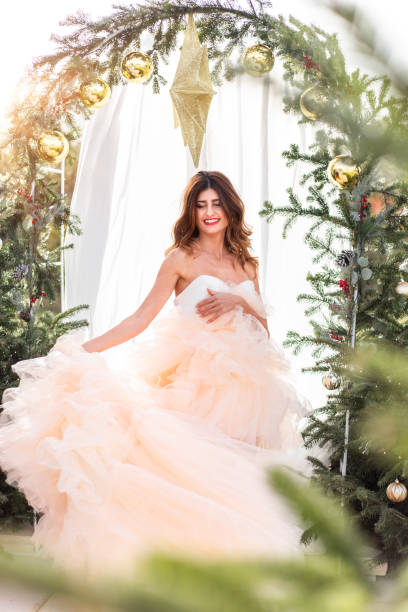 femme avec noël en robe élégante dans la mariée lumineuse de scène d’arbre de noël d’arbre de noël dans la lumière chaude du soleil pour le mariage de décembre - christmas wedding bride winter photos et images de collection