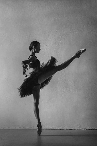 Young ballerina practicing dance moves on black background. Space for text