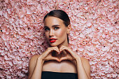 Beautiful emotional woman holding artificial showing heart sign against the background of a flower wall