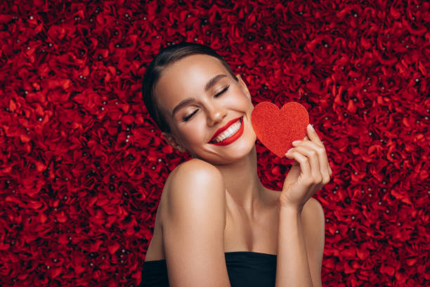 Beautiful emotional woman holding artificial heart against the background of a flower wall stock photo