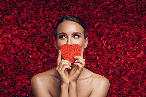 Beautiful emotional woman holding artificial heart against the background of a flower wall