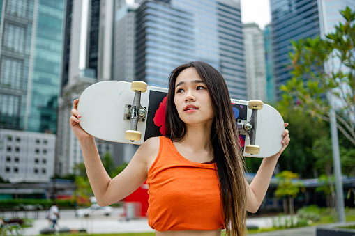 Confident young woman holding skateboard on shoulder, posing in the city, weekend activities concept