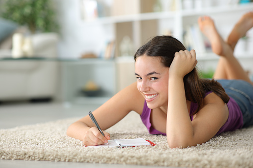 Happy woman at home writing in agenda looking at you