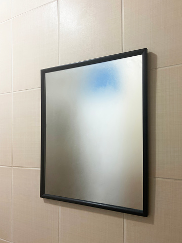 Foggy mirror hanging on tiled wall in bathroom