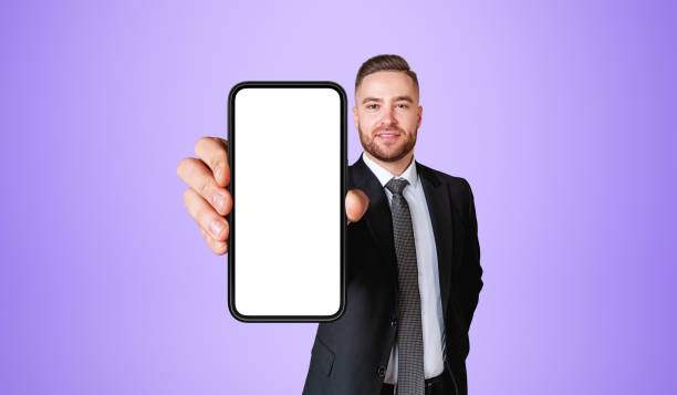 istock Smiling bearded businessman showing smartphone with blank screen, purple 1816198656