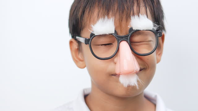 Boy wearing clown glasses fake nose mustache and eyebrows looks at camera and makes a facial expression.