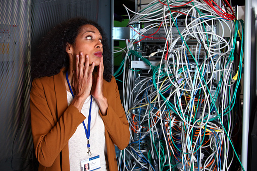 Computer rack in computer center full of wires. Big mess. Despair on a face of the woman.