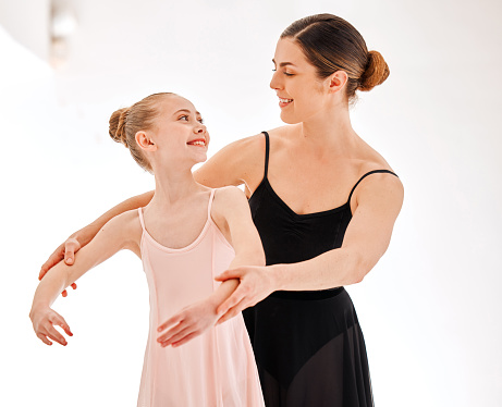 Ballet, learning class and dance teacher with child student in studio for dancing, art and coaching. Girl smile with woman ballerina coach or dancer to learn balance and academy performance with arms