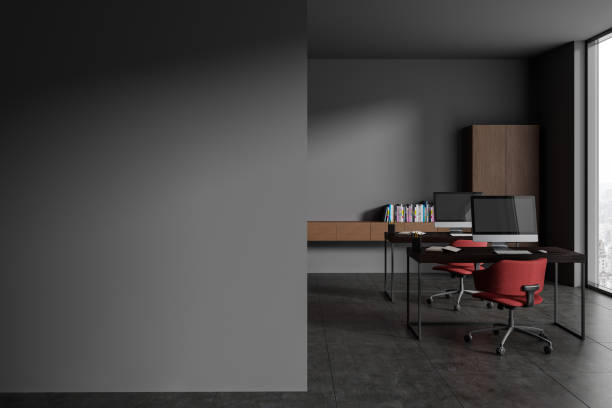 istock Grey office interior with pc monitors on table and shelf with window. Mock up wall 1816240803