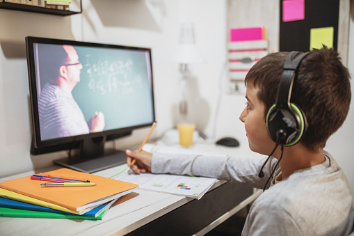 Distance learning online education. Caucasian smile kid boy studying at home with computer and doing school homework. Thinking child siting with notebook, pencils and training books. Back to school.