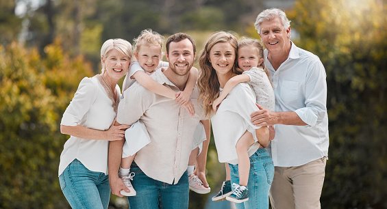 Portrait of multi-generation family standing together. Extended caucasian family smiling while spending time together at the park on a sunny day. Family with two children, parents and grandparents