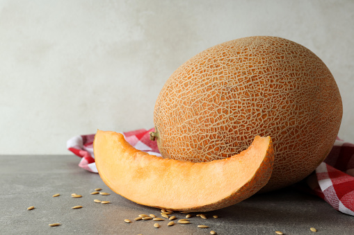 Ripe melon on gray textured table with kitchen towel