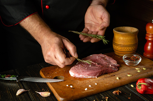 The cook adds dry aromatic rosemary to the meat steak. The process of cooking beef meat or shish kebab on the kitchen table with spices.