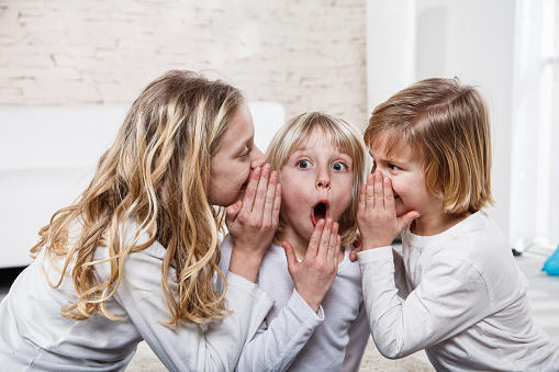 Three children gossip. Two are whispering on one's ears. The information is a shock.