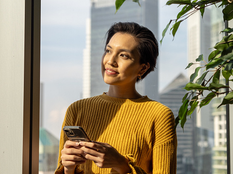 Business People - Portrait of a beautiful Asian Chinese female in yellow cardigan with her phone