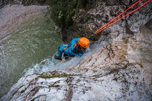 A Hispanic man in his mid-adult years, clad in a neoprene suit and safety helmet, enjoys the thrill of sliding down the canyon.