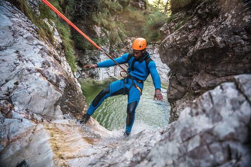 a black male, suited up in neoprene and helmet, conquers the canyons with bold descents while canyoning.