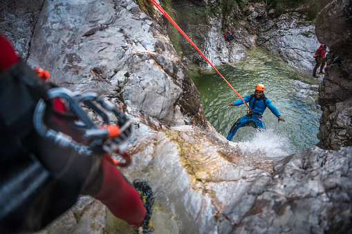 The excitement of canyoning, a black male, confidently navigating rocky terrain in a neoprene suit and helmet.