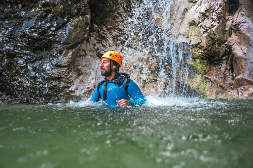 A mid-adult Hispanic male, equipped in a neoprene suit and helmet, takes on the challenges of canyoning.