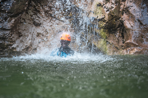 Canyoning experience, a black female in a neoprene suit and helmet stands beneath a waterfall, capturing the essence of adventure.