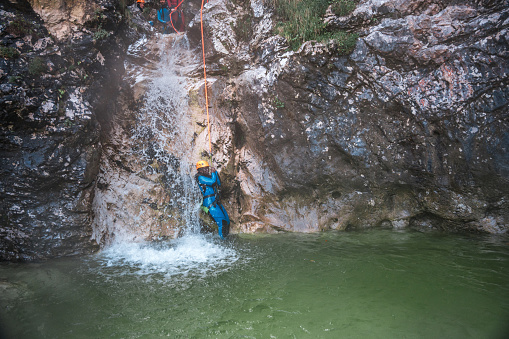 The excitement of canyoning, a black female, confidently sliding down in a neoprene suit and helmet.