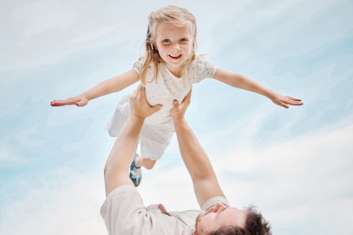 Low angle portrait of an adorable little caucasian girl being carried by her fun playful father while outside in a garden. Smiling cute daughter bonding with her dad in the backyard. Playing aeroplane