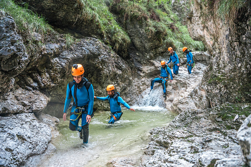 A diverse group, dressed in neoprene suits and safety helmets, moves around and has fun in the dynamic environment of canyoning.