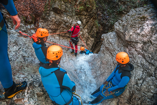 Diverse participants,  in neoprene suits and safety helmets, move around and enjoy every moment of their canyoning adventure.