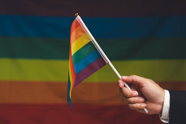 bandera del arco iris en la mano contra un fondo de la bandera del arco iris - homosexual gay pride business rainbow fotografías e imágenes de stock