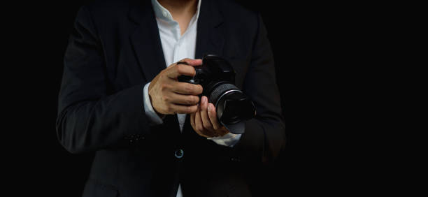 istock Photographer in a suit holding the digital camera while standing on a black background 1816316784