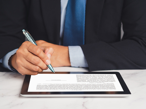 Signature electronic. A Businessman in a suit signing a digital contract or agreement on a tablet while sitting in the office. Business and technology concept