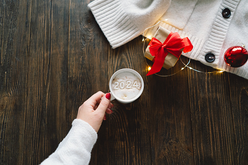 Happy New Year 2024 holidays drink, woman holding white coffee cup with number 2024. Christmas cup of coffee. Holiday atmosphere. Winter mood, holiday decoration