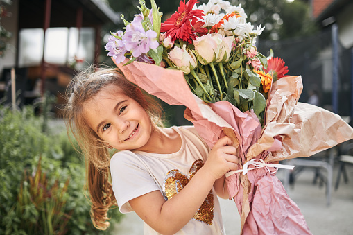 Girl is holding flower arrangement, ready to give it to her mother on mother’s day.