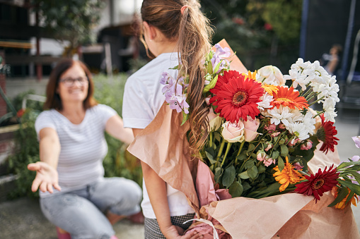Girl is holding flower arrangement behind her back, ready to give it to her mother on mother’s day.
