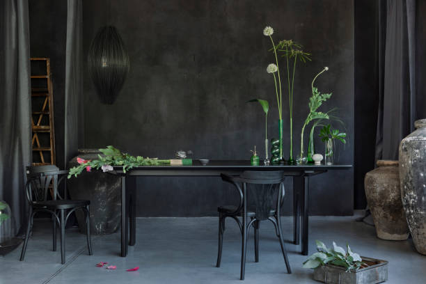 istock Creative composition of japandi dining room interior with black table, glass vase with green leaves, chair, stylish lamp, concrete wall and personal accessories. Home decor. Template. 1816343749