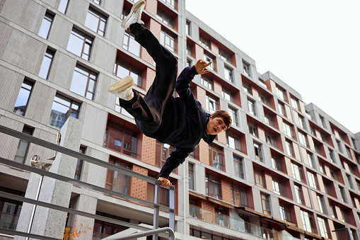 Athlete man, young guy jumping, flips of wall in public park among high-rise buildings over sunrise in action. Eye fish filter. Concept of lifestyle, extreme kinds of sport, freestyle, activity. Ad